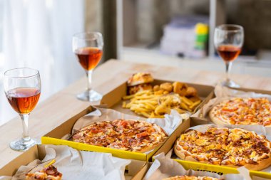 Meslektaşlar pizza partisinde öğle yemeği yer, çeşitli pizzalar yer ve kırsal ahşap masada kırmızı şarap içerek fast food öğle yemeğini kutlarlar.