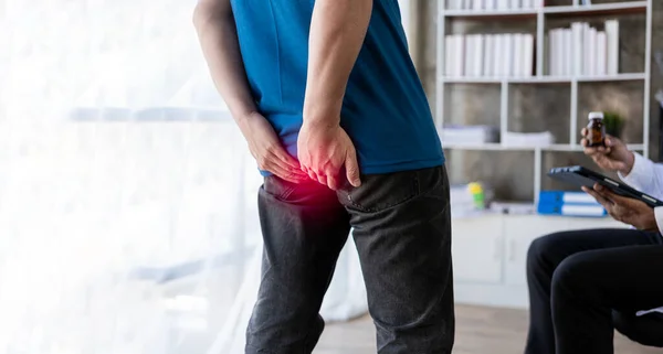 stock image Young man suffering from hemorrhoids consulting a doctor Man touching her buttocks because of abdominal pain and hemorrhoids health care concept