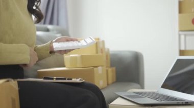 Asyalı iş kadını çevrimiçi satış yapıyor ve dizüstü bilgisayardan, telefondan sipariş alıyor ve nakliye paketleriyle ilgili notlar alıyor. İçişleri Bakanlığı kadın girişimcisi (KOBİ))