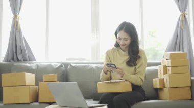 Asyalı iş kadını çevrimiçi satış yapıyor ve dizüstü bilgisayardan, telefondan sipariş alıyor ve nakliye paketleriyle ilgili notlar alıyor. İçişleri Bakanlığı kadın girişimcisi (KOBİ))