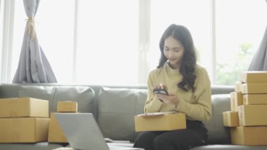 Asyalı iş kadını çevrimiçi satış yapıyor ve dizüstü bilgisayardan, telefondan sipariş alıyor ve nakliye paketleriyle ilgili notlar alıyor. İçişleri Bakanlığı kadın girişimcisi (KOBİ))