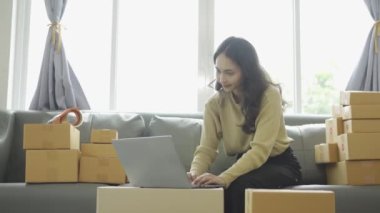 Asyalı iş kadını çevrimiçi satış yapıyor ve dizüstü bilgisayardan, telefondan sipariş alıyor ve nakliye paketleriyle ilgili notlar alıyor. İçişleri Bakanlığı kadın girişimcisi (KOBİ))