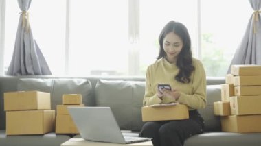 Asyalı iş kadını çevrimiçi satış yapıyor ve dizüstü bilgisayardan, telefondan sipariş alıyor ve nakliye paketleriyle ilgili notlar alıyor. İçişleri Bakanlığı kadın girişimcisi (KOBİ))