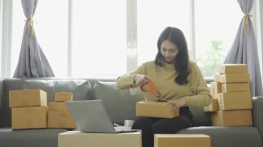 Asyalı iş kadını çevrimiçi satış yapıyor ve dizüstü bilgisayardan, telefondan sipariş alıyor ve nakliye paketleriyle ilgili notlar alıyor. İçişleri Bakanlığı kadın girişimcisi (KOBİ))