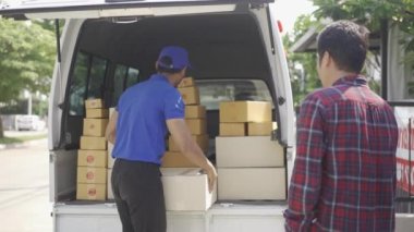 Postacı eve güler yüzlü ve mutlu bir yüzle paket getiriyor, Asyalı adam kapıdaki postacıdan kutu alıyor, ev teslimatı konsepti. 4k video.