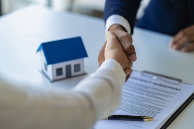 Emlakçı ve müvekkil el sıkışması ev sigortası üstüne ev sözleşmesi. Model evin arkasındaki inşaat sahasında proje kontratına başlamak için. Ev kredisi kavramı.
