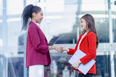 İş ortakları ofisinin önünde el sıkışıyor iki genç iş kadını anlaşma ya da ortaklık için el sıkışıyor. Gülümseyen Afrikalı kadına odaklan.