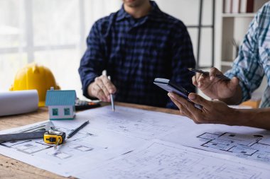 İnşaat şantiyesi mühendisleri, iki işadamı, mühendislik objeleri birbiriyle etkileşen ortaklar, müteahhitler ve mimarlarla birlikte dizüstü bilgisayardaki planlara bakıyorlar ve proje üzerinde çalışma hakkında konuşuyorlar.