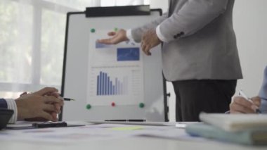 İşletme grafiği grafiğine işaret eden muhasebeci, haritadaki mali iş raporuna işaret ederek, ortaklarıyla birlikte bir başarı stratejisi planlamak için çalıştıkları bir proje üzerinde beyin fırtınası düzenliyor.