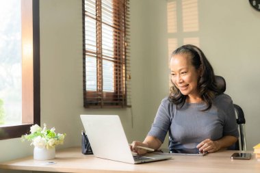 60 'lı yaşlarda bir iş kadını dizüstü bilgisayar kullanarak masada oturuyor. Evde çalışan orta yaşlı bir kadın sosyal medyada internet üzerinden buluşup sohbet ediyor..