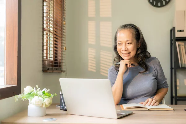 An old businesswoman in her sixties sitting at a table using a laptop. middle aged woman working at home Meet and chat online using the internet on social media.