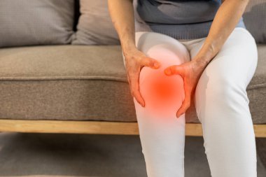 Yaşlı bir kadın, mutsuz yaşlı bir kadının kanepe profilinde otururken dizini acıdan tutuyor. Üzücü. Üzgünsün. Acıyor. Yaralı diz. ilaç