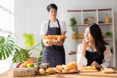 Asyalı erkek ve kadın sağlıklı bir kahvaltı hazırlamak için yemek ve ekmek hazırlıyorlar. Keyifle yemek pişirmek, büyüleyici bir eş ve neşeli bir koca taze malzemelerle enfes yemekler hazırlıyor..