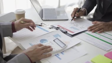 Asyalı işadamı, iş yerindeki bir ekiple fikir paylaşımı ve iş analizi yapıyor. Turta grafikleri ve istatistiklerle belgeleri paylaşıyorlar. 