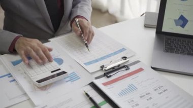 Asyalı işadamı, iş yerindeki bir ekiple fikir paylaşımı ve iş analizi yapıyor. Turta grafikleri ve istatistiklerle belgeleri paylaşıyorlar. 