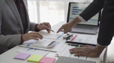 Asyalı işadamı, iş yerindeki bir ekiple fikir paylaşımı ve iş analizi yapıyor. Turta grafikleri ve istatistiklerle belgeleri paylaşıyorlar. 