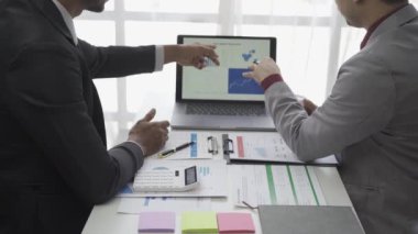 Asyalı işadamı, iş yerindeki bir ekiple fikir paylaşımı ve iş analizi yapıyor. Turta grafikleri ve istatistiklerle belgeleri paylaşıyorlar. 