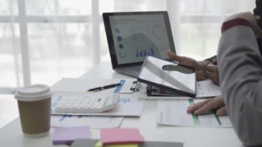 Asyalı işadamı, iş yerindeki bir ekiple fikir paylaşımı ve iş analizi yapıyor. Turta grafikleri ve istatistiklerle belgeleri paylaşıyorlar. 