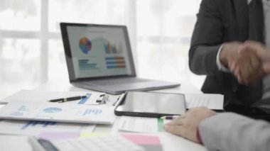 Asyalı işadamı, iş yerindeki bir ekiple fikir paylaşımı ve iş analizi yapıyor. Turta grafikleri ve istatistiklerle belgeleri paylaşıyorlar. 