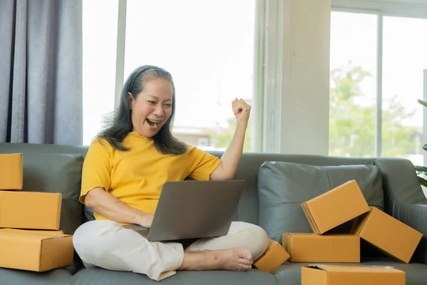 Successful old businesswoman smiling happily receiving new buzzer Asian woman owns a small business online with shipping boxes. concept of working at home