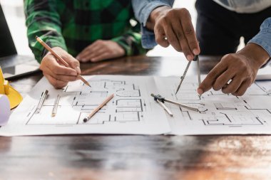 Sarı elbiseli iki mühendis çalışıyor ve beyaz büyük planı tartışıyorlar. İki meslektaşı ofis masasındaki inşaat alanında mimari projeyle veri ve dizüstü bilgisayarları tartışıyorlar.
