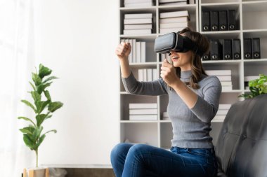 VR kulaklıklı genç Latin kadının havaya dokunmasına şaşırdım. Gözlüklü gülümseyen beyaz kadın sanal gerçeklik teknolojisi aygıtı koltukta otururken 3D simülasyon videosu izliyor..