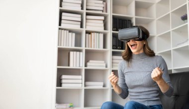 VR kulaklıklı genç Latin kadının havaya dokunmasına şaşırdım. Gözlüklü gülümseyen beyaz kadın sanal gerçeklik teknolojisi aygıtı koltukta otururken 3D simülasyon videosu izliyor..
