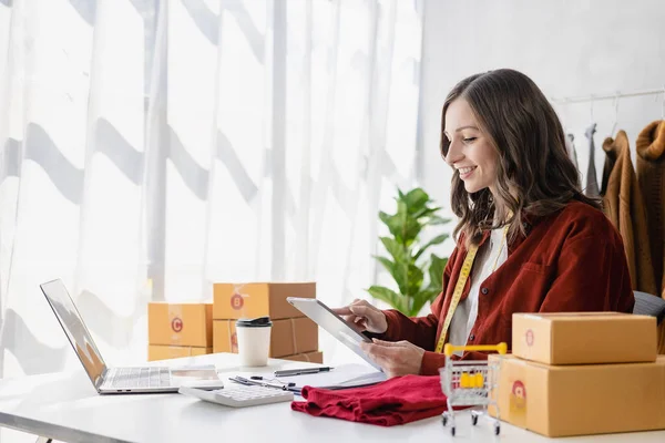 Small Business Startup, SME, Female Entrepreneur Owner uses smartphone or tablet to take and verify online orders to prepare boxes and deliver parcels.