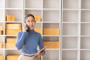 Küçük Girişim, KOBİ, Girişimci - Akıllı telefon veya dizüstü bilgisayar kullanan mutlu Asyalı kadın, kutu hazırlamak ve çevrimiçi siparişleri iletmek için çevrimiçi siparişleri alır ve onaylar.