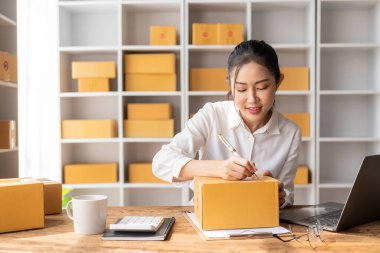 Küçük bir işletme kurmak KOBİ İş Sahibi Asyalı kadın girişimci fatura kutuları üzerinde çalışır ve çevrimiçi sipariş veren müşterilere satılık kutular hazırlamak için çevrimiçi siparişleri işaretler.