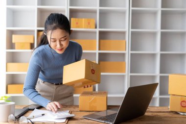 starting a small business SME Business Owner Asian female entrepreneur works on receipt boxes and checks online orders to prepare boxes for sale to customers who order online. clipart