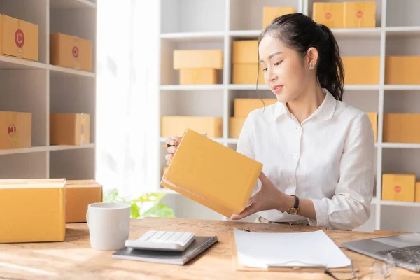 starting a small business SME Business Owner Asian female entrepreneur works on receipt boxes and checks online orders to prepare boxes for sale to customers who order online.