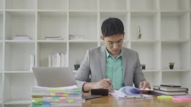 Ofiste çalışan Asyalı erkek işadamı bilgisayarınızı ve hesap makinenizi kullanarak mali raporları hesaplıyor. Finansal muhasebe kavramında