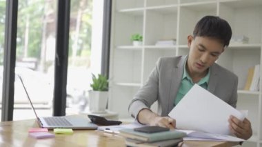 Ofiste çalışan Asyalı erkek işadamı bilgisayarınızı ve hesap makinenizi kullanarak mali raporları hesaplıyor. Finansal muhasebe kavramında