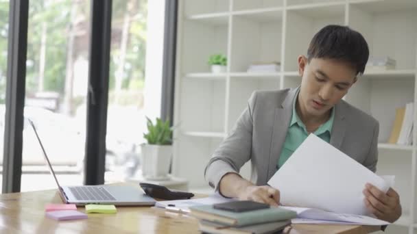 在办公室工作的亚洲男性商人利用你的笔记本电脑和计算器来计算财务报告管理文档 在财务会计概念中的作用 — 图库视频影像