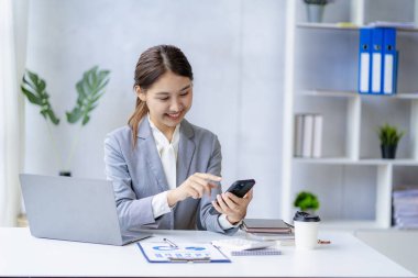 Gülümseyen Asyalı kadın müşteriyle konuşuyor. Genç, pozitif kadın muhasebeci akıllı telefon kullanıyor. Masasındaki ekiple konuşuyor.