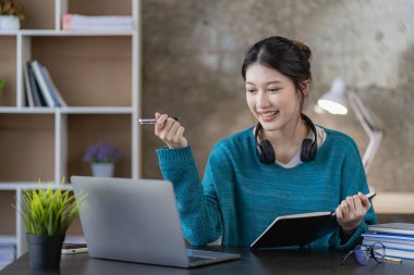 Asyalı bir lise öğrencisi evde dizüstü bilgisayarla ders öğreniyor ve izliyor. Genç kız öğrenci evde öğretmeniyle çevrimiçi sınıfta okuyor.