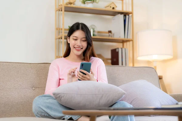 stock image Beautiful Asian woman in casual clothes sitting on sofa using smartphone for social entertainment to relax. smile and laugh