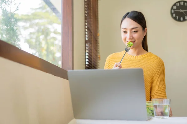 stock image Happy young Asian woman with fresh vegetables and fresh fruits, healthy concept working lunch at home, beautiful woman with laptop eating salad, lifestyle in living room concept.