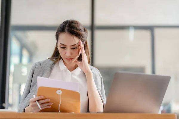 stock image Thinking Asian businesswoman looking at financial statements and making marketing plan using computer on her desk in office holding report papers girl reading financial information