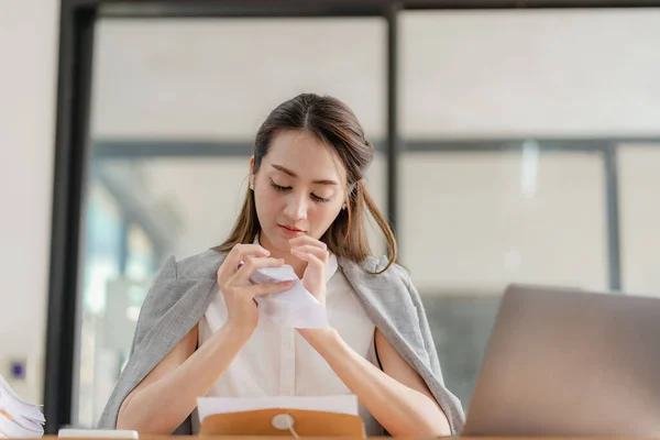 stock image Asian businesswoman in suit sitting on desk in office, with computer document graph for bookkeeping in workplace to calculate annual profit by function, business concept