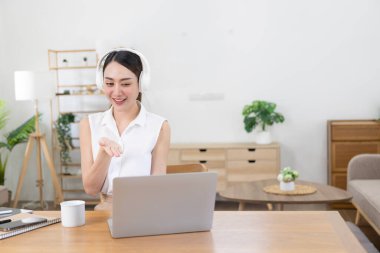 Kulaklık takan mutlu genç Asyalı kadın sosyal medya aracılığıyla dizüstü bilgisayarla sohbet ediyor..