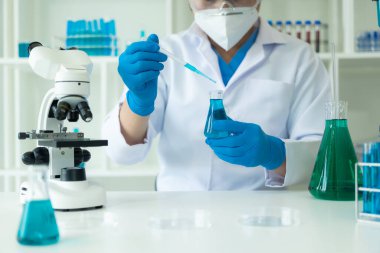 Eldivenli bir bilim adamı temiz sıvıyla test tüpüne mavi asit döküyor. Kimya endüstrisindeki bilimsel araştırmalar. Doktor analizi mikroskop ile test tüpünde inceliyor..