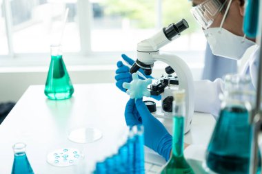 Eldivenli bir bilim adamı temiz sıvıyla test tüpüne mavi asit döküyor. Kimya endüstrisindeki bilimsel araştırmalar. Doktor analizi mikroskop ile test tüpünde inceliyor..