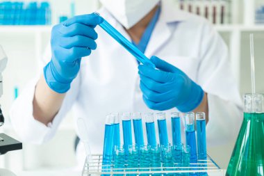Eldivenli bir bilim adamı temiz sıvıyla test tüpüne mavi asit döküyor. Kimya endüstrisindeki bilimsel araştırmalar. Doktor analizi mikroskop ile test tüpünde inceliyor..