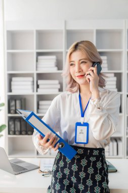 Asyalı genç bayan çalışan akıllı telefon kullanarak müşterilere danışmanlık yapıyor. İş danışmanlığı kavramı dikey görüntü.