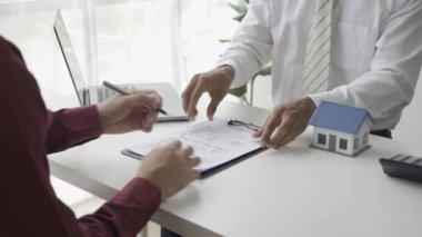 Ev alıcıları bir emlakçıyla ev kiralama ya da satın alma konusunda ve ev satın alma anlaşmasının şartları hakkında görüşür ve müşteriden satışı tamamlamak için evrakları imzalamasını isterler..