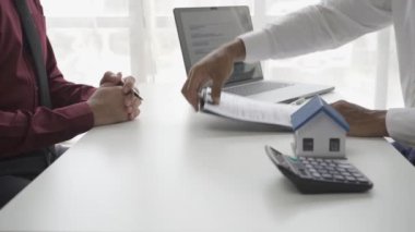 Ev alıcıları bir emlakçıyla ev kiralama ya da satın alma konusunda ve ev satın alma anlaşmasının şartları hakkında görüşür ve müşteriden satışı tamamlamak için evrakları imzalamasını isterler..