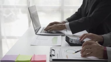 Belgede grafik verilerini analiz eden iki mali danışmanı olan Asyalı erkek işadamı bilgisayarınızda 4K bürosunda çalışan meslektaşlarınızla birlikte dosya ve belgeler oluşturun..