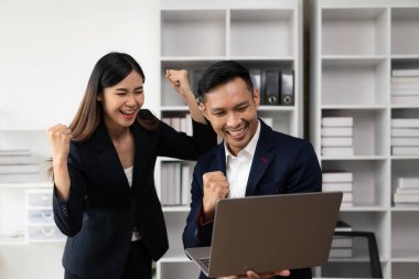 İki başarılı genç Asyalı iş adamı diz üstü bilgisayarlarıyla ellerini kaldırıyorlar. Zaferleri ve başarıları birlikte kutlayın. Modern ofiste el çırpın.